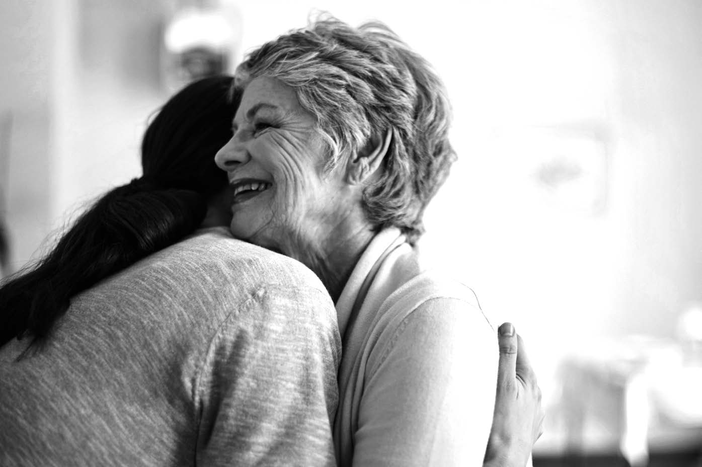 Black and white view of woman giving a hug to smiling older woman 